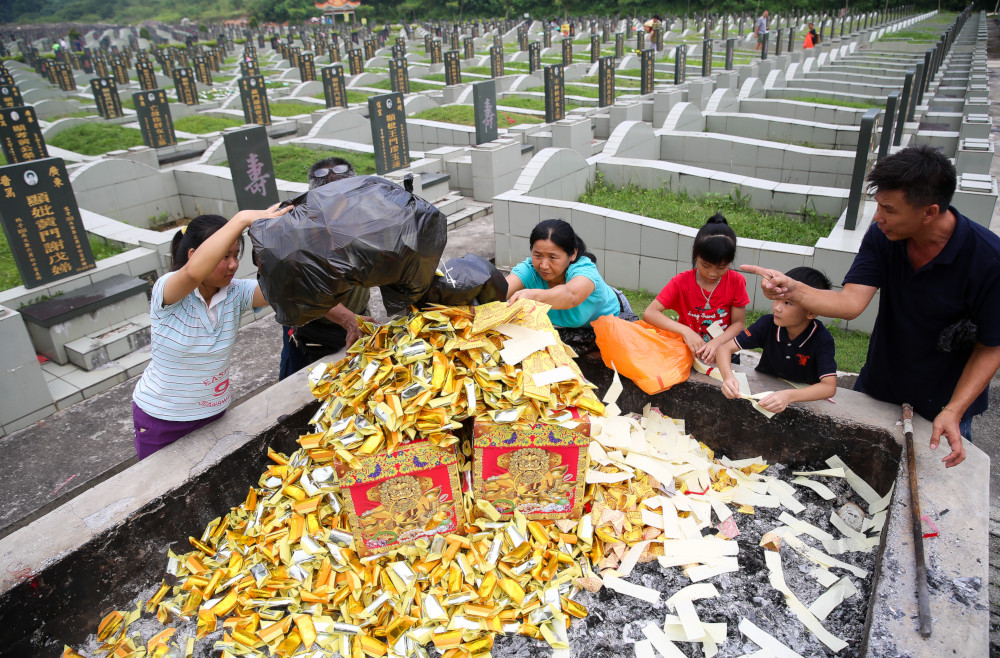 A family unloads bags of ‘hell money’ onto a grave at Kwong Tong Cemetery in Kuala Lumpur. — Picture by Choo Choy May