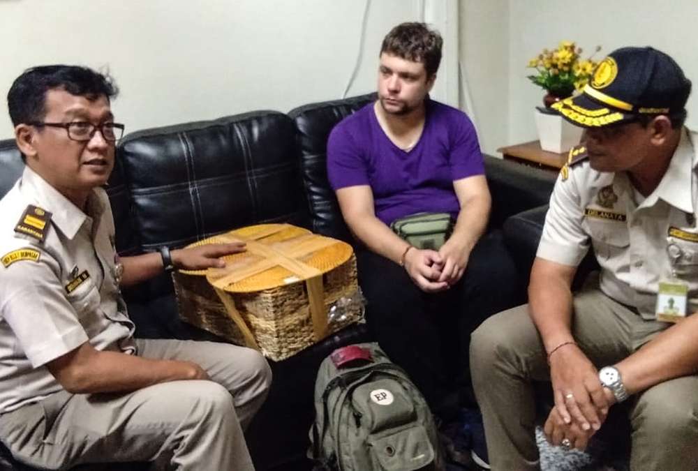 Russian national Andrei Zhestkov (centre) being held for smuggling a two-year-old orangutan in a rattan basket at Bali's international airport in Denpasar March 23, 2019. u00e2u20acu201d Natural Resources Conservation Agency of Bali handout via AFP