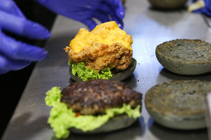 Assembling the patty and chicken thigh on the charcoal buns.