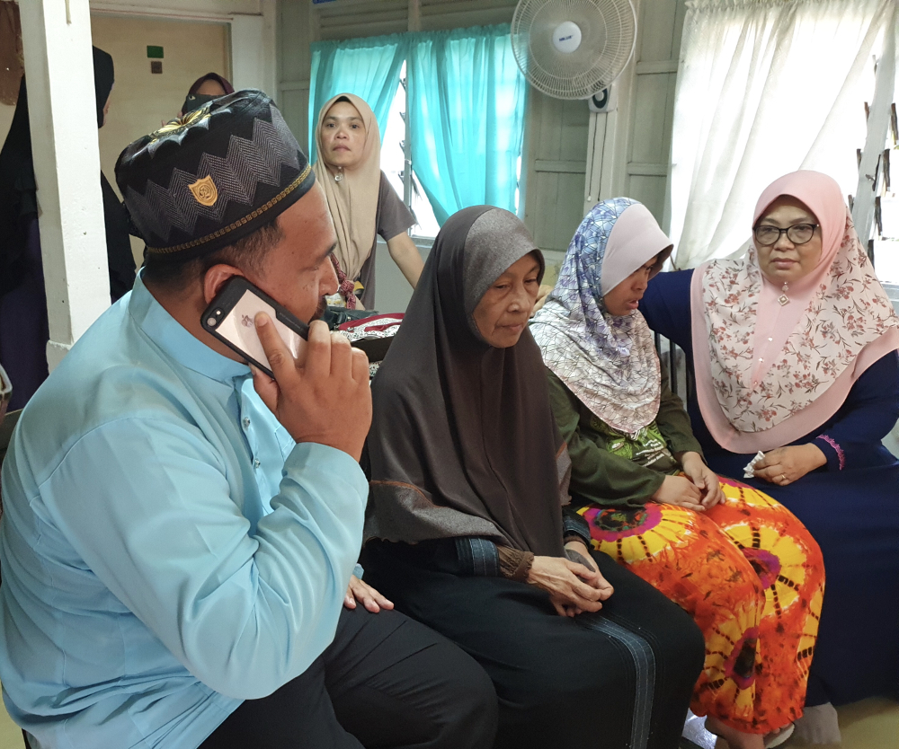 Bayan Lepas assemblyman Azrul Mahathir Aziz (left) speaking on the phone with Norazila as Rokiah (second from left) and relatives waited for updates Rahimi Ahmad. u00e2u20acu201d Picture by Opalyn Mok