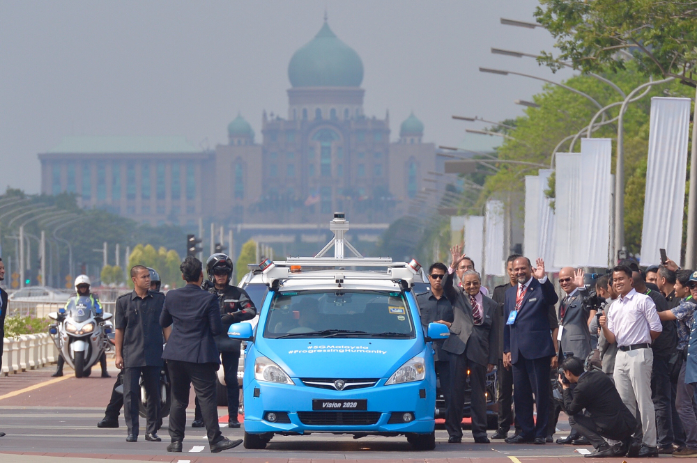 Prime Minister Tun Dr Mahathir Mohamad and Communication and Multimedia Minister Gobind Singh Deo wave at the crowd as they stand next to the 5G autonomous car.