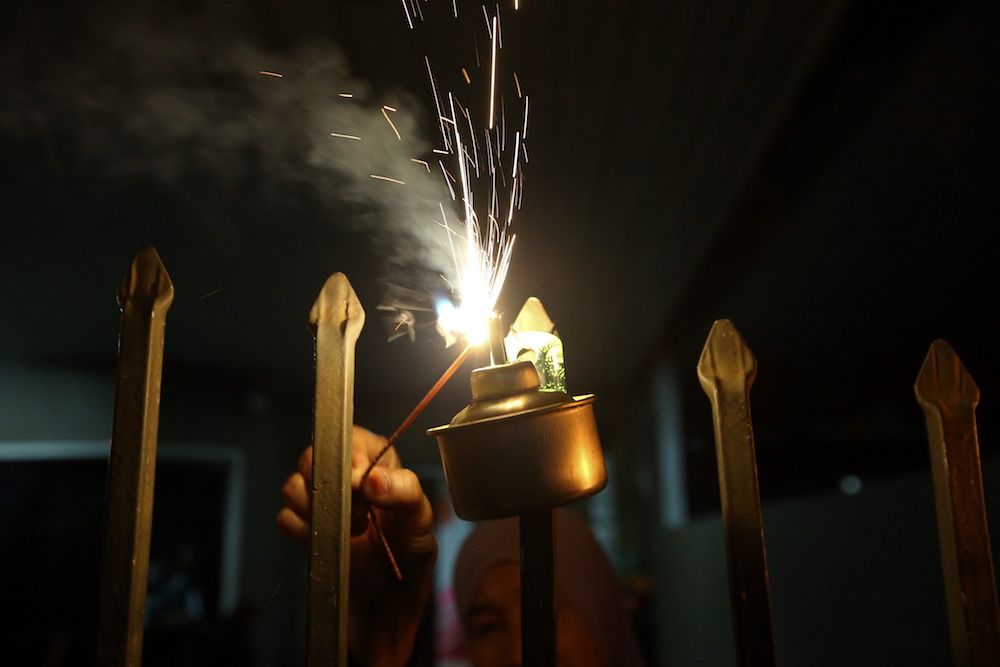 A man lights an oil lamp with a sparkler in Taman Siakap, George Town June 12, 2018. u00e2u20acu201d Picture by Sayuti Zainudin