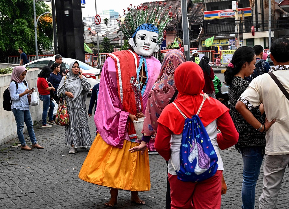 This picture taken on March 16, 2019 shows a child operating a brightly coloured folk effigy known as Ondel-ondel to make a living on the streets of Jakarta. — AFP pic