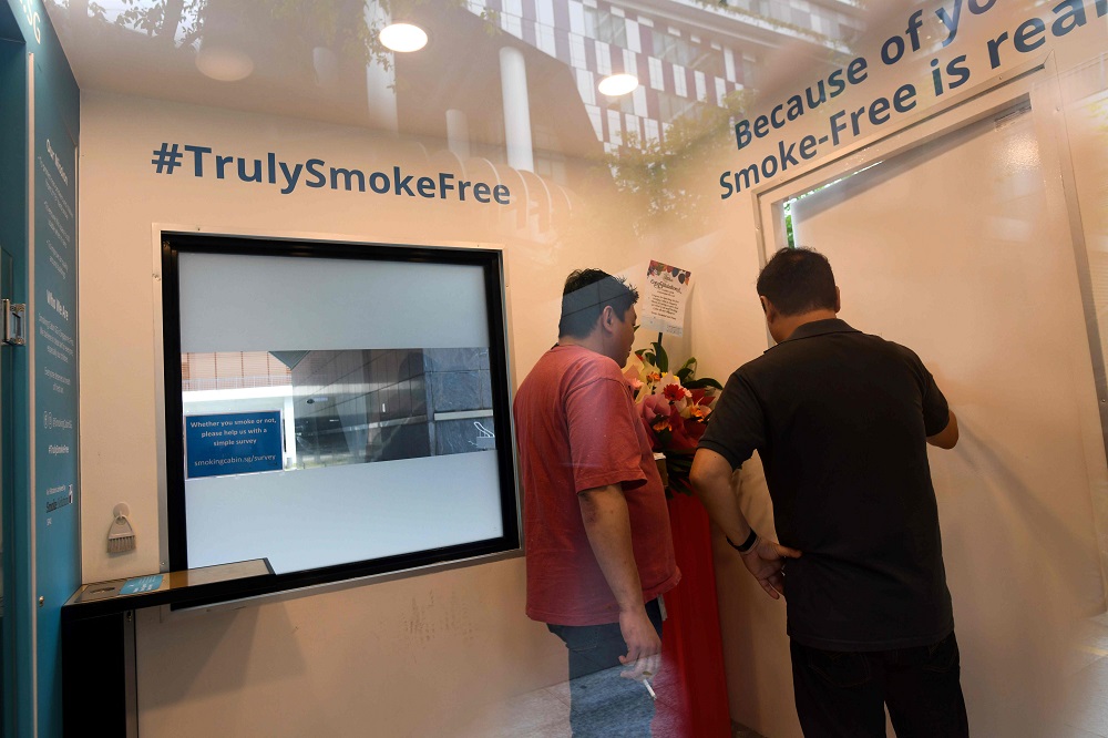 People smoke inside a smoking cabin, developed by Southern Globe Corporation, outside an office building in Singapore May 22, 2019. — AFP pic