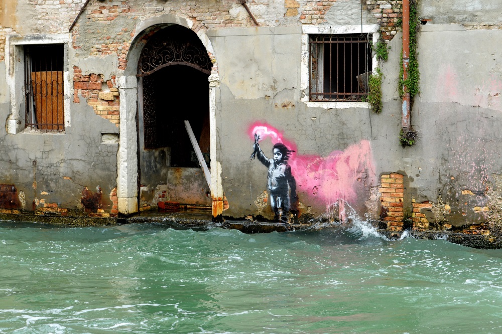 An alleged work by British street artist Banksy depicting a migrant child wearing a lifejacket holding a pink flare, is painted on the outer wall of a house overlooking the canal Rio de Ca Foscari, in Venice May 21, 2019. u00e2u20acu201d AFP pic