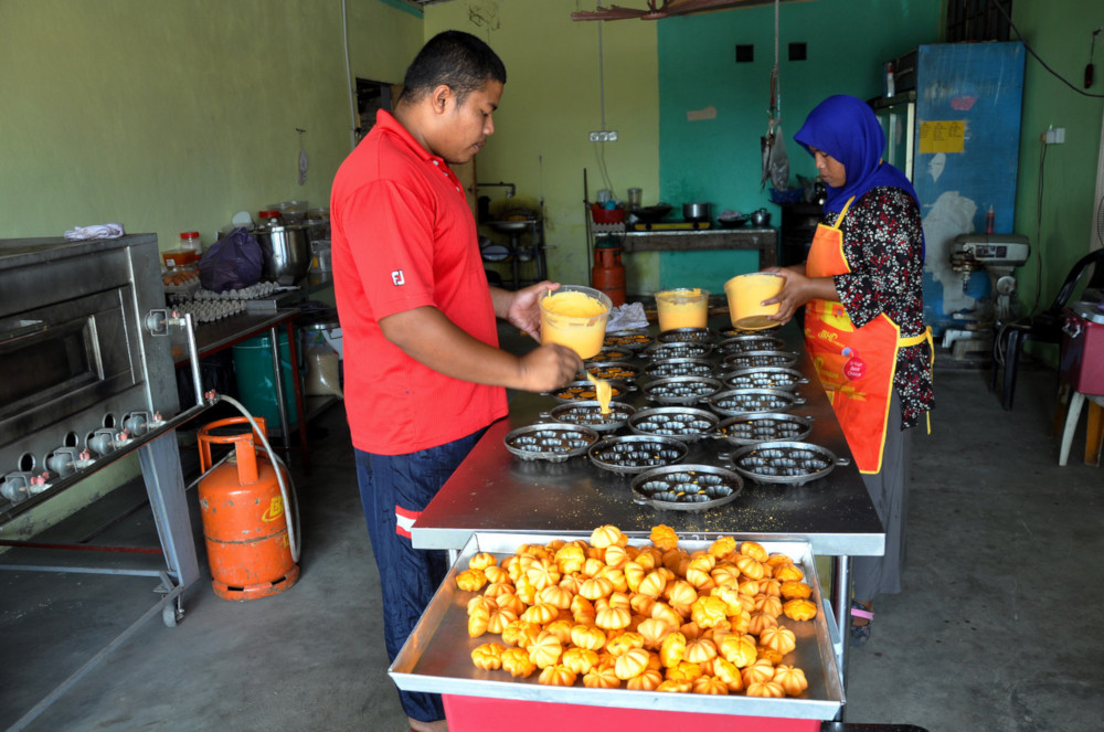 ‘Nekbat’ entrepreneur Fadhilah Abd Ghani (right) and her brother Mohd Shaiful Bhari place ‘nekbat’ batter into moulds before it is baked in the oven. — Bernama pic 