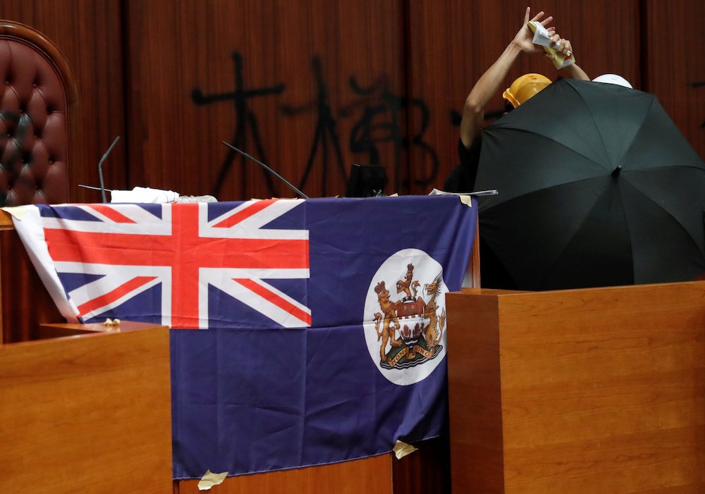 A person tears a book of Hong Kong Basic Law as he stands next to a colonial flag of Hong Kong displayed inside a chamber in Hong Kong July 1, 2019. u00e2u20acu201d Reuters picnn
