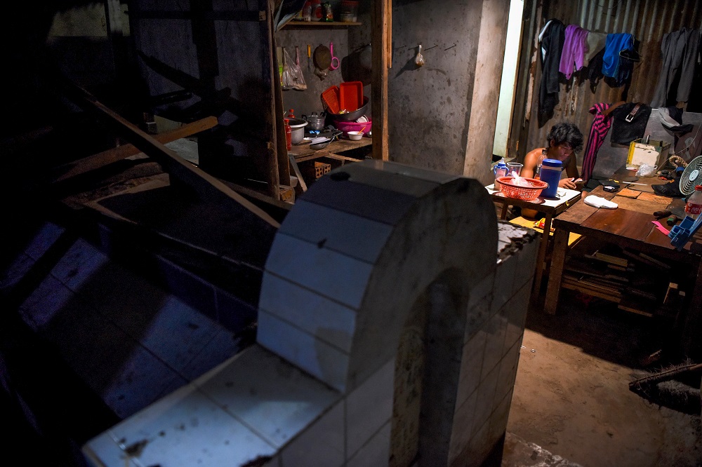 This picture taken on May 21, 2019 shows a man using his mobile phone in his home beside a grave in Phnom Penh. — AFP pic