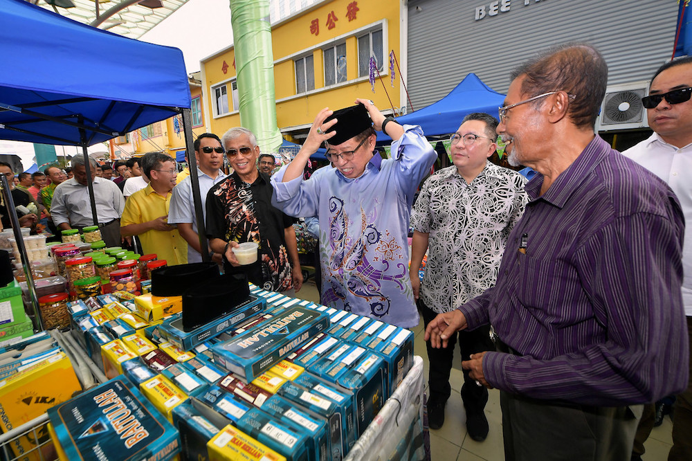 Chief Minister Datuk Patinggi Abang Johari Openg tries on a songkok while officiating the Gawai Raya Street Bazaar in Kuching May 25, 2019. u00e2u20acu201d Bernama pic
