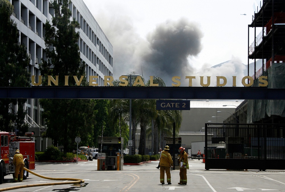A fire truck and firefighters are seen at Gate 2 of Universal Studios as smoke rises (background) from a fire that rages out of control at the backlot filled with movie sets in Universal City, California June 1, 2008. u00e2u20acu201d Reuters pic     