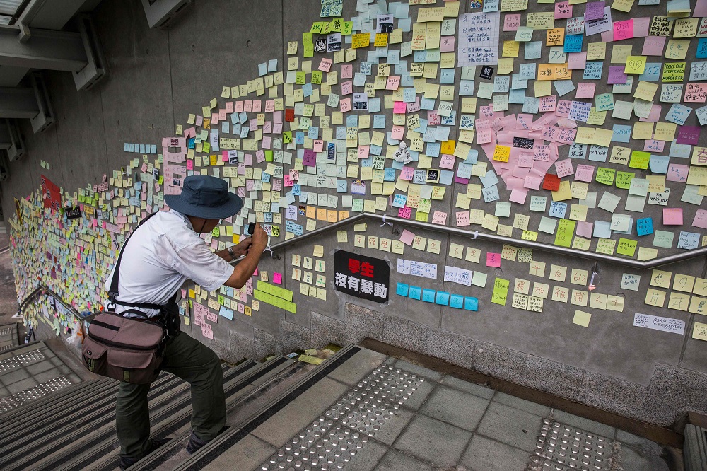 This picture taken on June 22, 2019 shows a man taking photographs of artwork and messages in support of protesters opposed to a China extradition law posted on the u00e2u20acu02dcLennon Wallu00e2u20acu2122 outside the government headquarters in Hong Kong. u00e2u20acu2022 AFP pic        