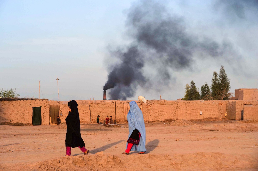 In this photograph taken on April 3, 2019, Afghan women walk near a brick factory as smoke rises up in the sky from a chimney on the outskirts of Jalalabad. u00e2u20acu201d AFP pic       