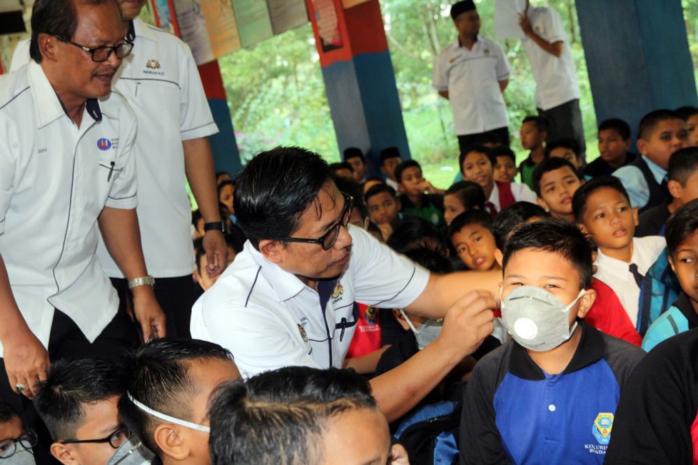 Johor Education Department director Azman Adnan helps a school student put on a breathing mask in Pasir Gudang June 30, 2019. u00e2u20acu201d Bernama pic