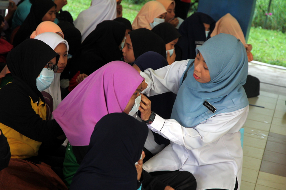 A teacher from SK Pasir Gudang 4 helps a student put on a face mask in Pasir Gudang, Johor June 30, 2019. u00e2u20acu201d Bernama pic