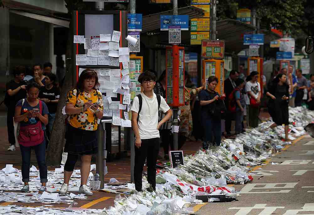 Commuters wait for buses at a bus stop next to a memorial site with flowers placed to honour a man who died after falling from a scaffolding at the Pacific Place complex while protesting the extradition bill, in Hong Kong June 17, 2019. u00e2u20acu201d Reuters pic