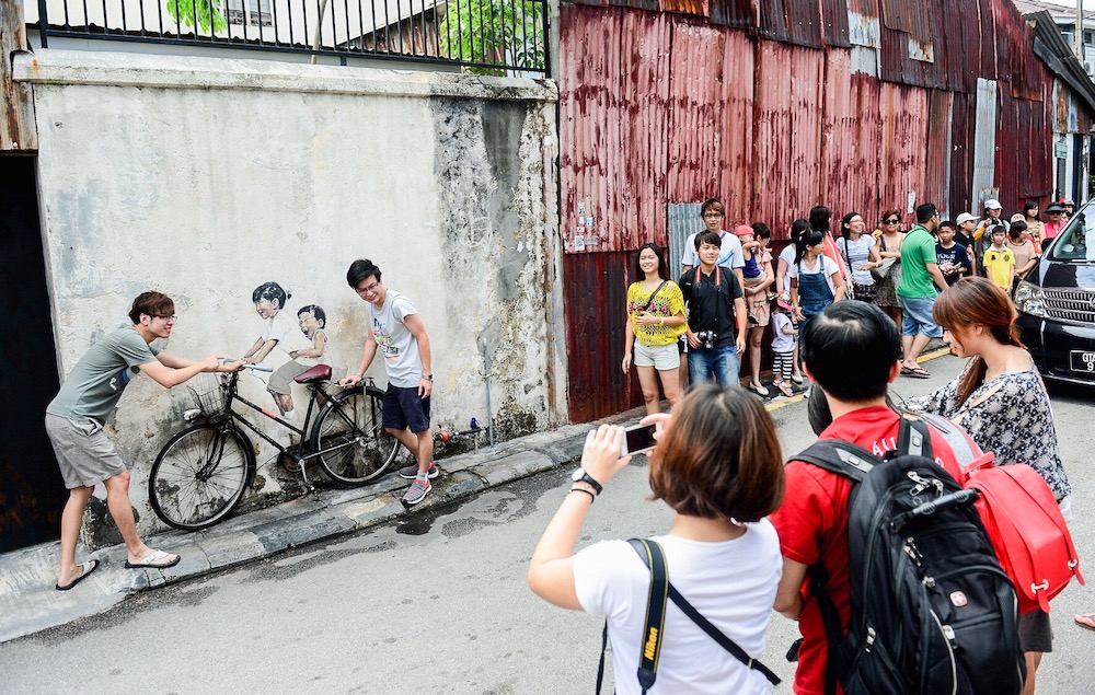 Tourists line up to take photos with the famous Little Children on a Bicycle mural by Ernest Zacharevic at Lorong Armenian in Georgetown. u00e2u20acu201d Picture by Azrol Ali