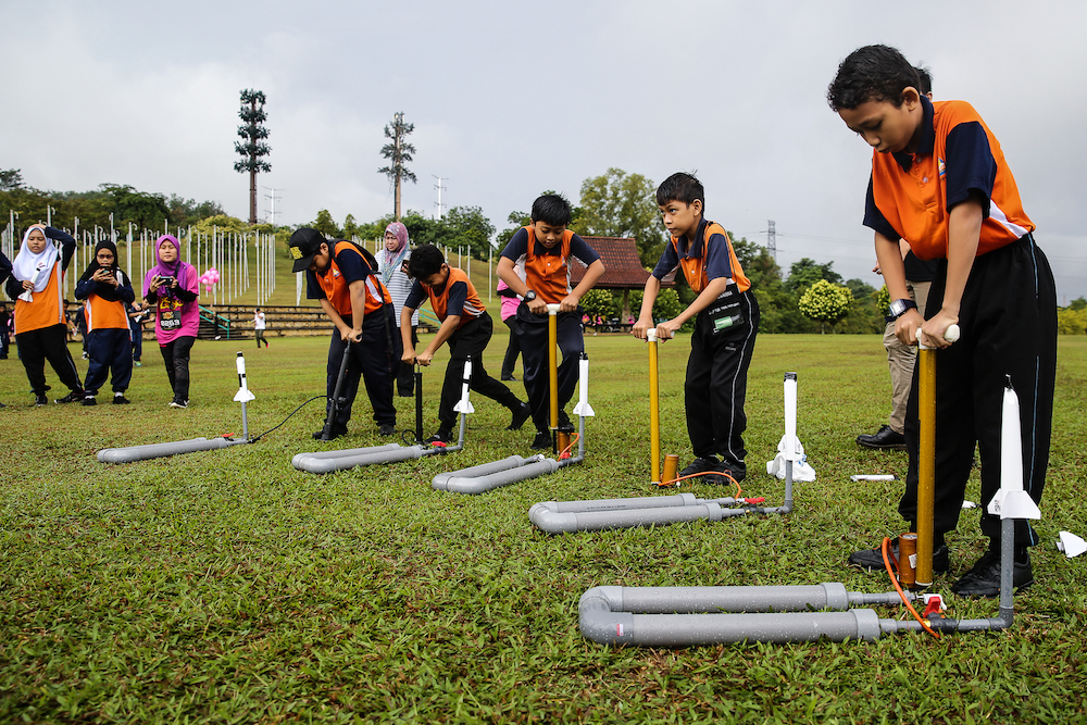 Students using a pump to raise the air pressure before launching their handmade rockets into the sky. — Picture by Yusof Mat Isa.