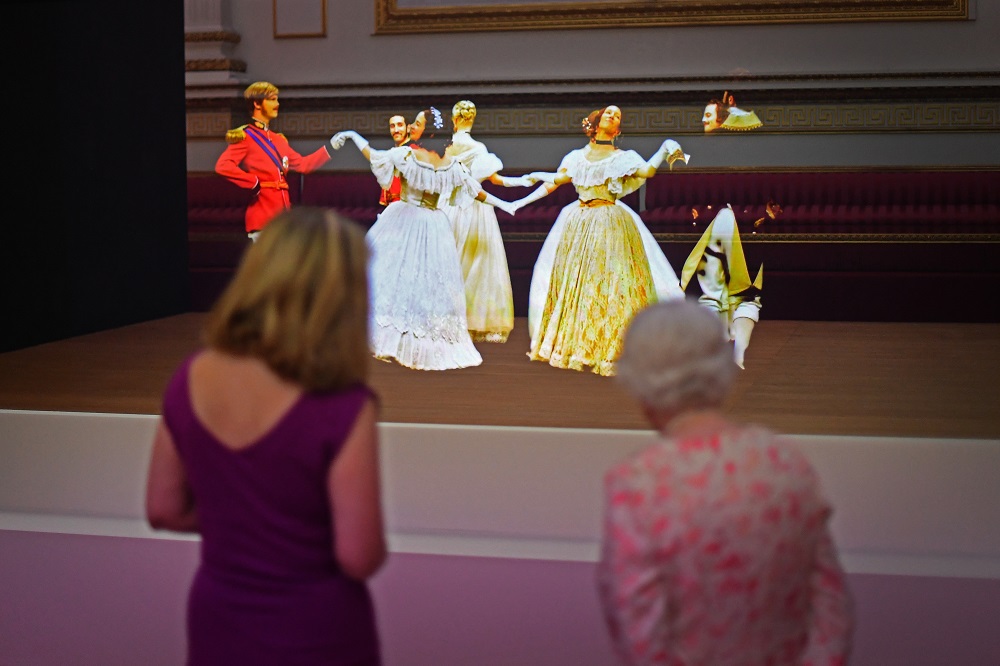 Queen Elizabeth II looks at a Pepperu00e2u20acu2122s Ghost illusion of a waltz danced at the 1856 Crimean Ball, part of an exhibition to mark the 200th anniversary of Queen Victoriau00e2u20acu2122s birth, for the summer opening of Buckingham Palace, London July 17, 2019. u00e2u20acu201d AFP