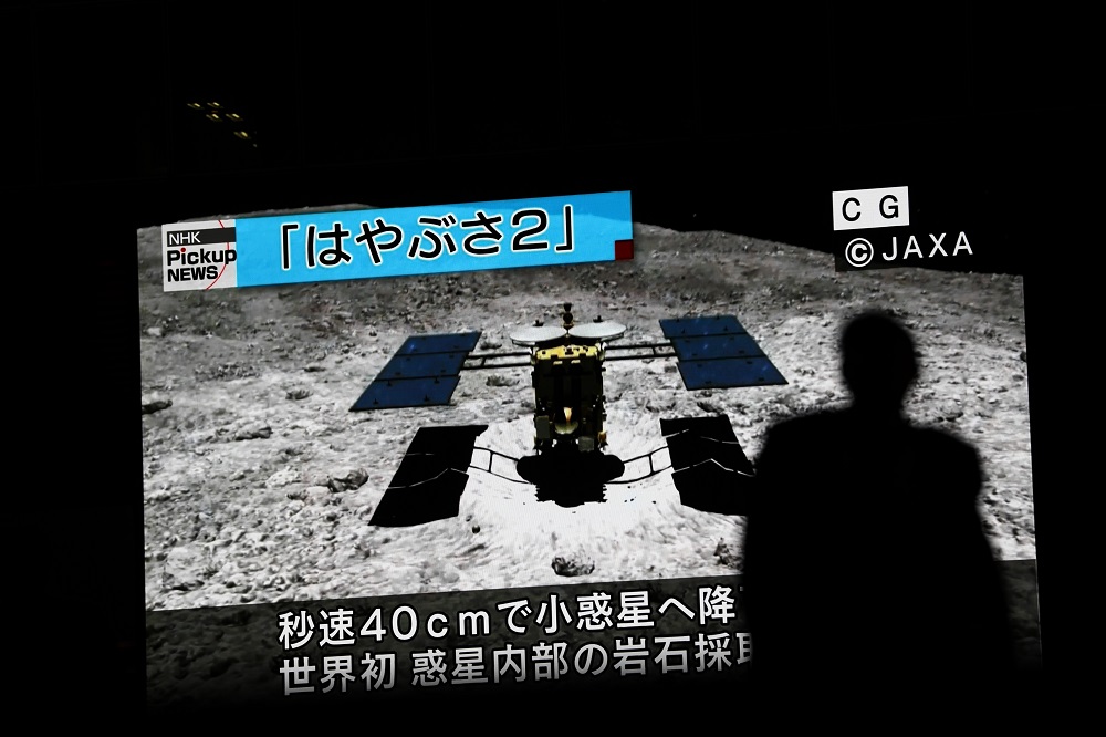 In this picture taken on July 10, 2019 a man walks past a screen displaying a computer-generated image of the Hayabusa2 probe, during a news broadcast at Akihabara district in Tokyo. u00e2u20acu201d AFP pic       