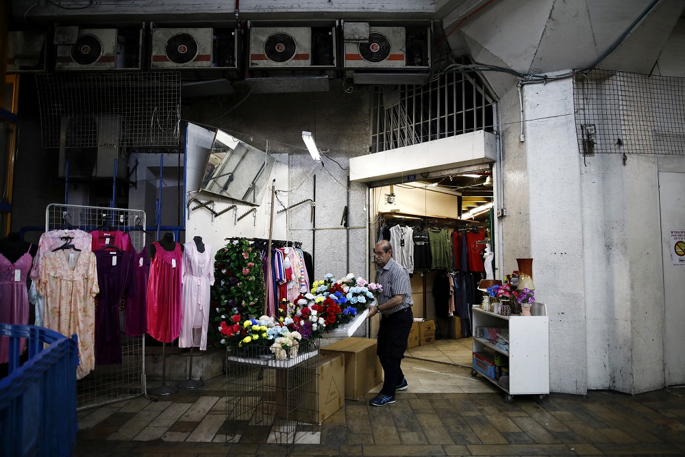 A vendor carries plastic flower decorations out of a shop as he prepares to open the store at the Central Bus Station in Tel Aviv, Israel May 29, 2019. — Reuters pic