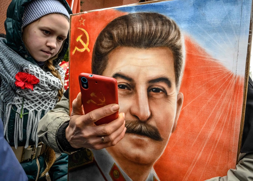 A woman, next to a girl, holds a portrait of Soviet leader Joseph Stalin and takes a selfie at his grave outside the Kremlin on the Red Square in Moscow on March 5, 2019. u00e2u20acu201d AFP pic         
