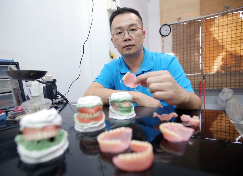 Loh and some of his masterpieces with samples of dentures in various stages of completion. u00e2u20acu2022 Picture by Fahan Najib