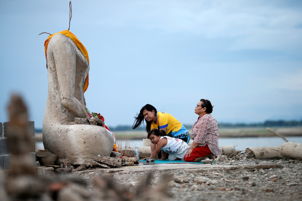 A family prays near the ruins of a headless Buddha statue, which has resurfaced in a dried-up dam due to drought, in Lopburi August 1, 2019. u00e2u20acu201d Reuters pic