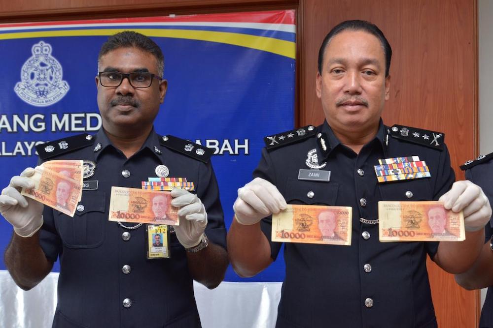 Zaini (right) holding up some of the fake Brazilian reals seized from the suspect last Monday. u00e2u20acu201d Picture by Julia Chann