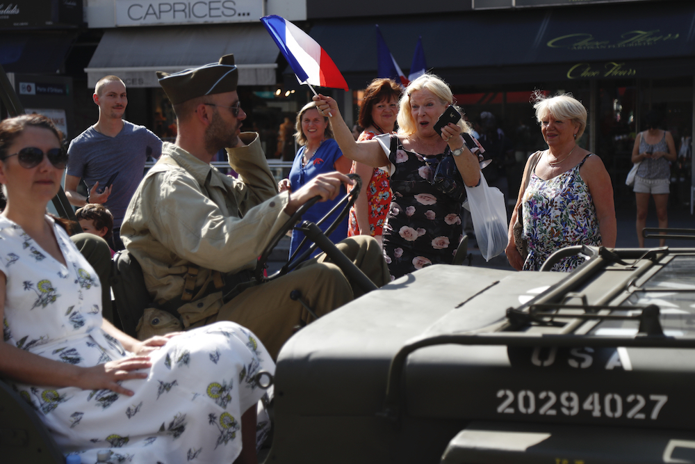 A woman waves a French flag as she looks at people wearing period uniforms taking part in the 'Freedom parade' as they re-enact celebrations of the liberation of Paris in Paris. u00e2u20acu201d AFP pic