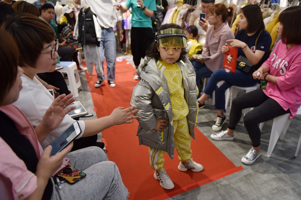 This photo taken on May 9, 2019 shows a child model posing as a buyer checks the quality of clothing at a fashion show for buyers in a children's clothing store in Beijing.  — AFP pic