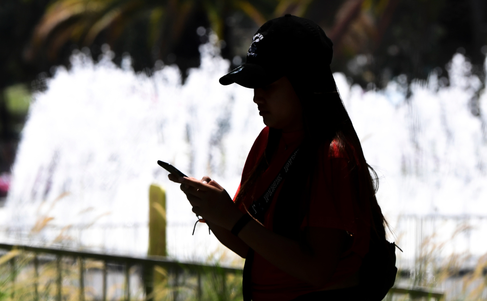 A woman uses her cellphone while walking past a water fountain in Los Angeles, California August 13, 2019. US retailers and global financial markets got an early Christmas present as President Donald Trumpu00e2u20acu2122s administration announced it is delaying tarif