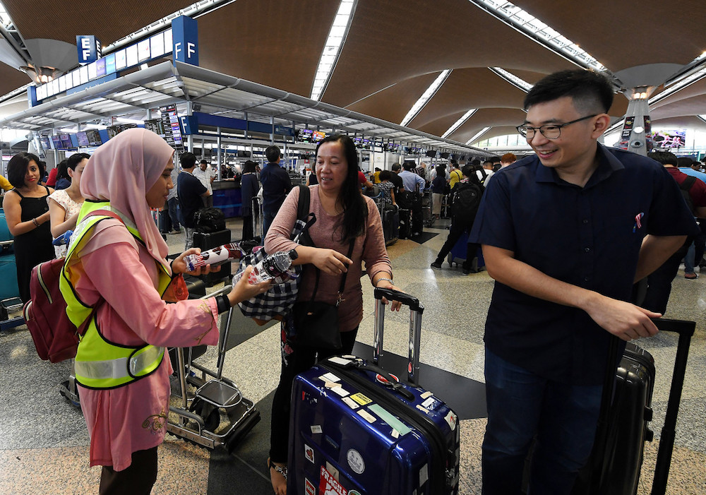 A MAHB member of staff distributes water and snacks to passengers at KLIA in Sepang August 23, 2019. — Bernama pic