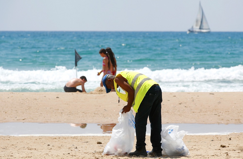 An employee of the Herzliya town hall collects plastics and other waste left behind by beachgoers, on one of the beaches of the coastal city June 21, 2019. ― AFP pic          
