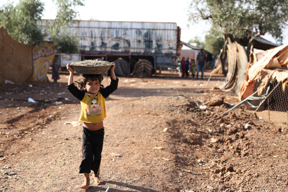 A child walks carrying a basin over the head on a footpath by a field at a camp for displaced Syrians near the village of Shamarin, near the border with Turkey in the northern Syrian Aleppo province, August 5, 2019. u00e2u20acu201d AFP pic