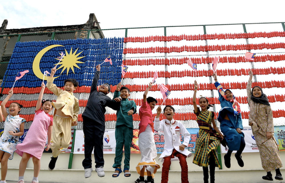 Penang students jump for joy in front of the national flag made out of recycled mineral water bottles. u00e2u20acu201d Bernama pic