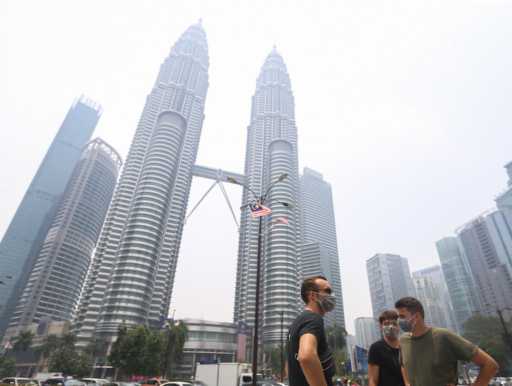 Tourists wear masks as they walk past the Petronas Twin Towers shrouded in haze in Kuala Lumpur September 12, 2019. u00e2u20acu201d Picture by Firdaus Latif