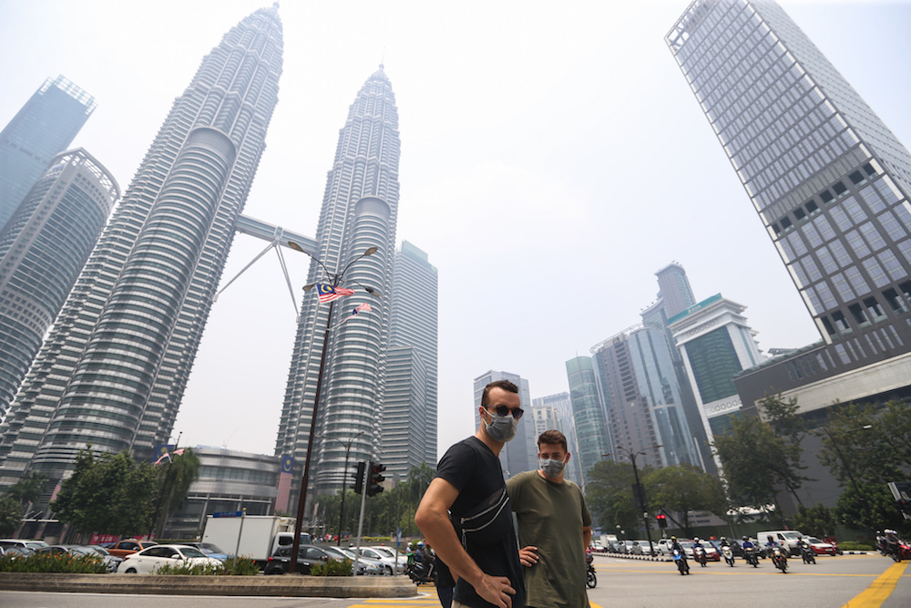 Tourists wear masks as they walk past the Petronas Twin Towers shrouded in haze in Kuala Lumpur September 12, 2019. u00e2u20acu201d Picture by Firdaus Latif