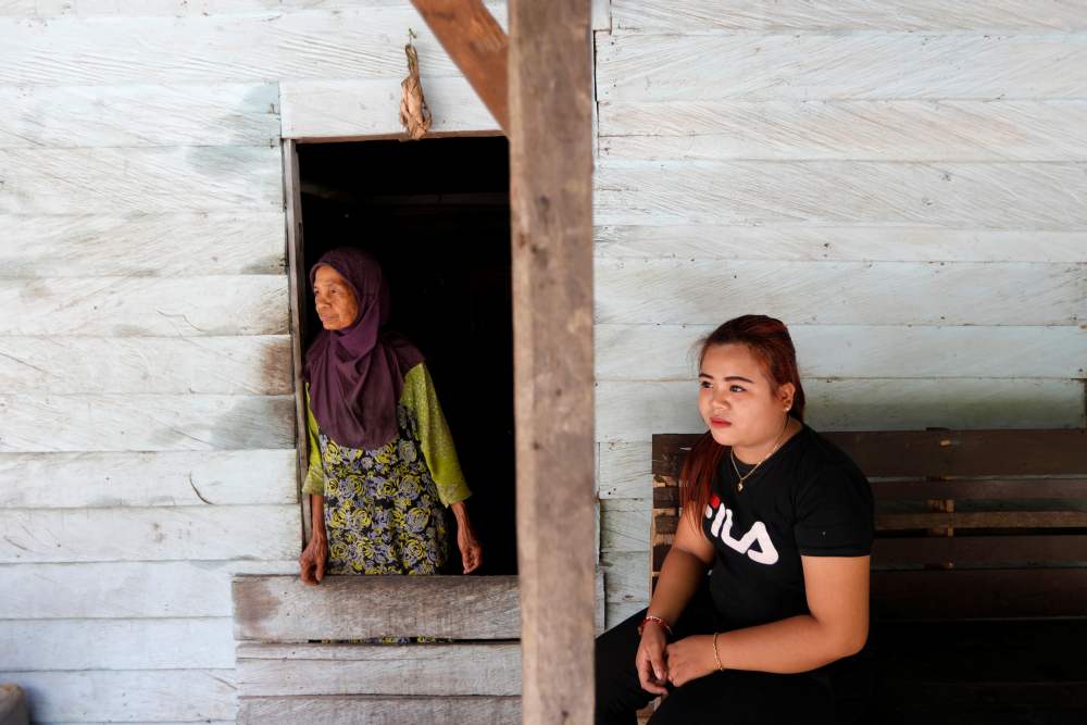 Ipah, who is a local resident in Semboja district, sits on a bench as her grandmother looks through a door at her stall near the main road at Samboja district in Kutai Kertanegara regency, East Kalimantan province, Indonesia August 29, 2019. u00e2u20acu2022 Reuters p