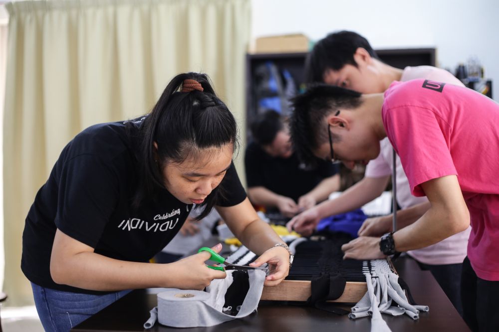 Vicki Tan helping out her fellow students perfect their woven floor mats. — Picture by Ahmad Zamzahuri