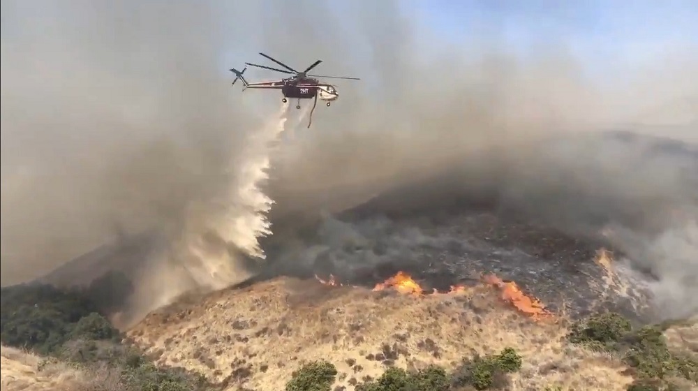 A helicopter makes a drop on the southern flank of fire in Simi Valley, California October 30, 2019, in this still image obtained from a social media video. u00e2u20acu201d Picture via Twitter/415Fire