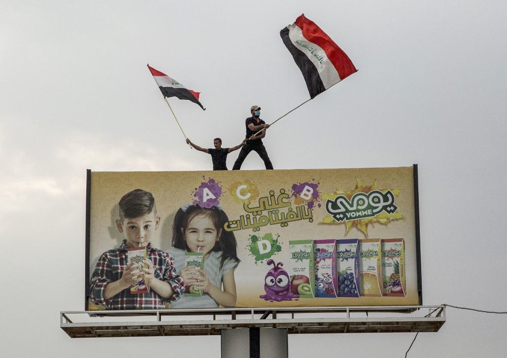 Iraqi protesters wave national flags as they stand atop a billboard during an anti-government demonstration outside the local government headquarters in the southern city of Basra on October 25, 2019. u00e2u20acu201d AFP pic