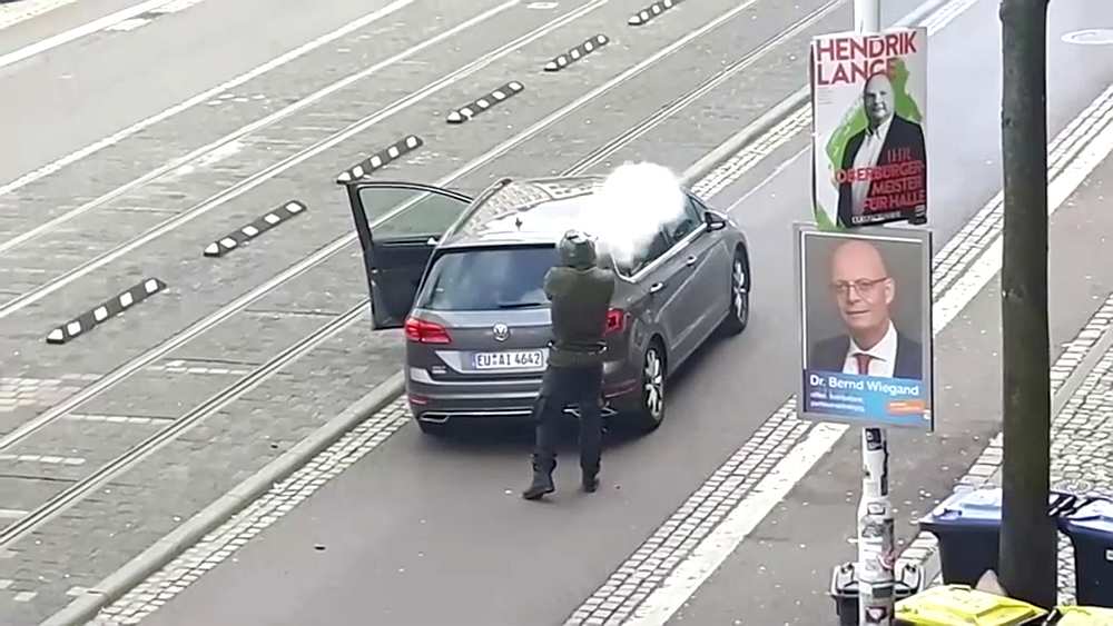 A man shoots a firearm from behind a grey car in Halle, Germany October 9, 2019. u00e2u20acu201d ATV Studio Halle/Reuters TV imagre via Reuters
