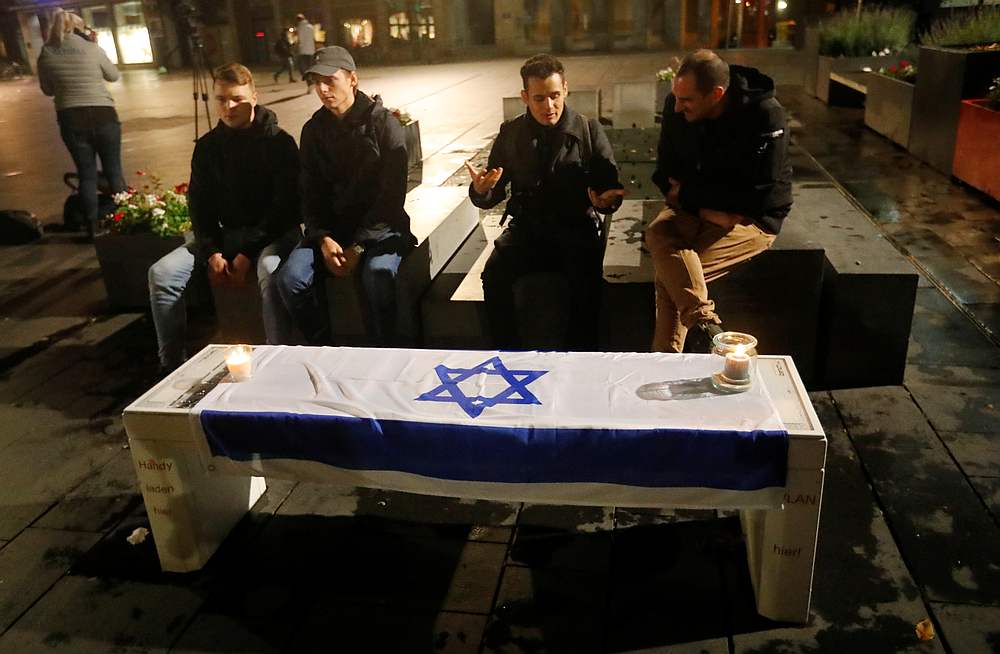People sit near an Israeli flag with lit candles on it at central market square in Halle, Germany October 9, 2019 after two people were killed in a shooting. u00e2u20acu201d Reuters pic