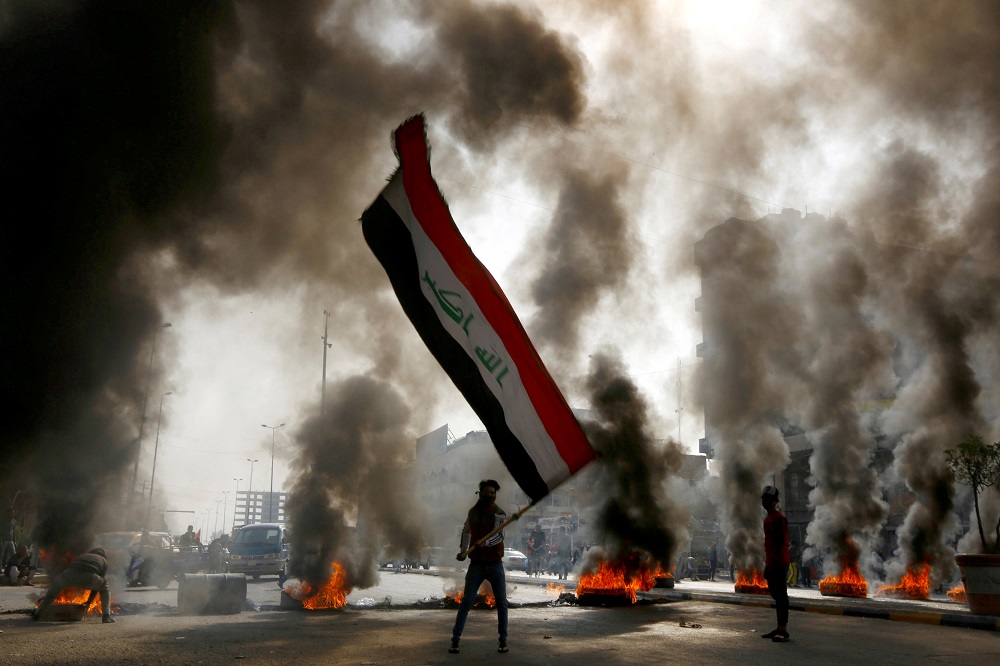 A protester holds an Iraqi flag amid a cloud of smoke from burning tires during ongoing anti-government protests in Najaf, Iraq November 26, 2019. u00e2u20acu201d Reuters pic