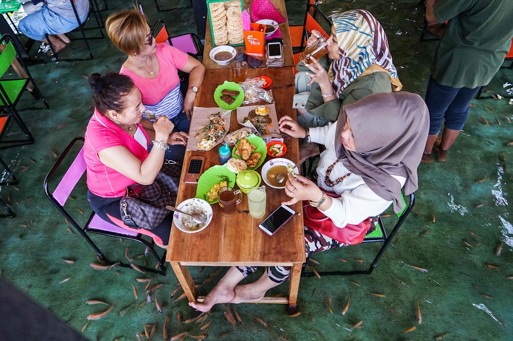 This picture taken on November 15, 2019 shows Indonesian diners having lunch while fish bite their feet at a fish pool restaurant at Wedomartani village in Yogyakarta. u00e2u20acu201d AFP pic  