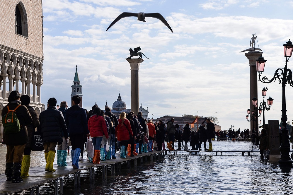People walk on a footbridge across the flooded St Mark’s Square by the statue of the Lion of St Mark (left) and the Column of St Theodore of Amasea (rear right) in Venice November 14, 2019. — AFP pic