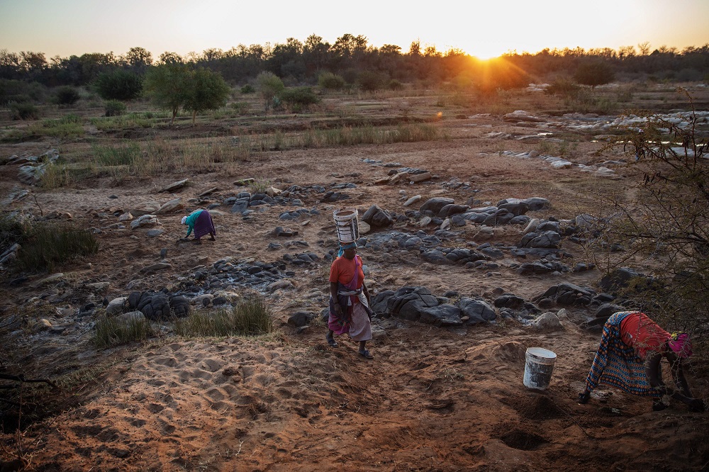Ndaheni Mashele, 66, (centre) carries a bucket containing water while Josephine Macete, 48, (left) and Basani Mathebula, 43, scratch the salt-rich soil from the riverbank of the Klein Letaba River near Baleni, in the South African province of Limpopo, in the early morning of August 26, 2019. — AFP pic