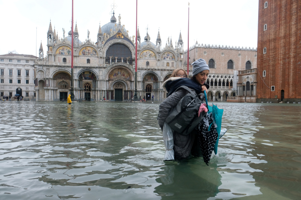 A woman carrying a child on her back wades in the flooded St Marku00e2u20acu2122s Square in Venice, Italy November 12, 2019. u00e2u20acu201d Reuters pic