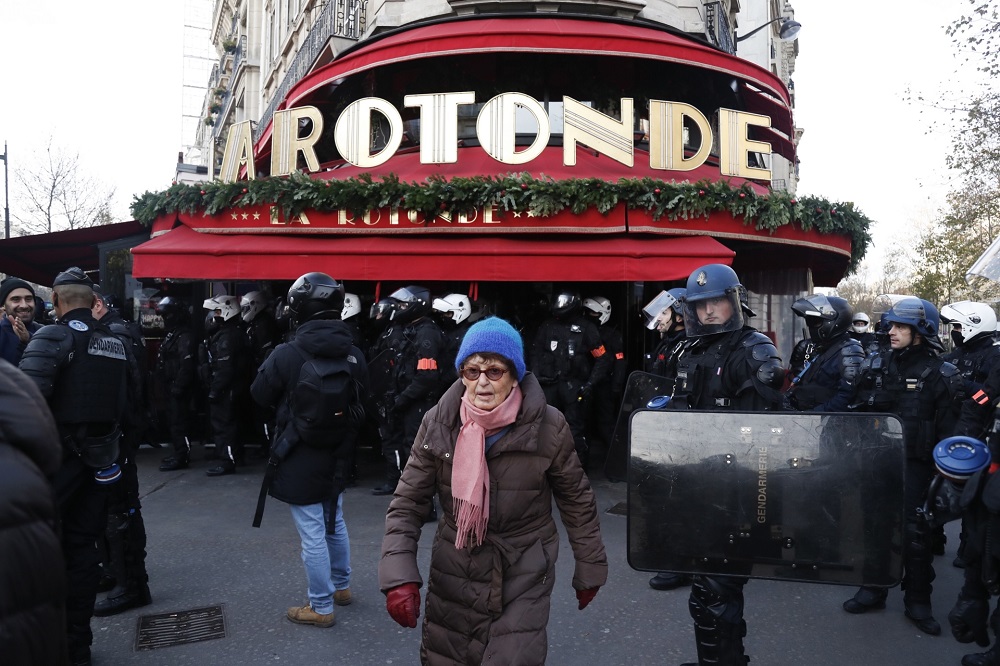 A woman walks past a riot police gendarme as people take part in a demonstration on December 10, 2019 next to La Rotonde in Paris. u00e2u20acu201d AFP pic