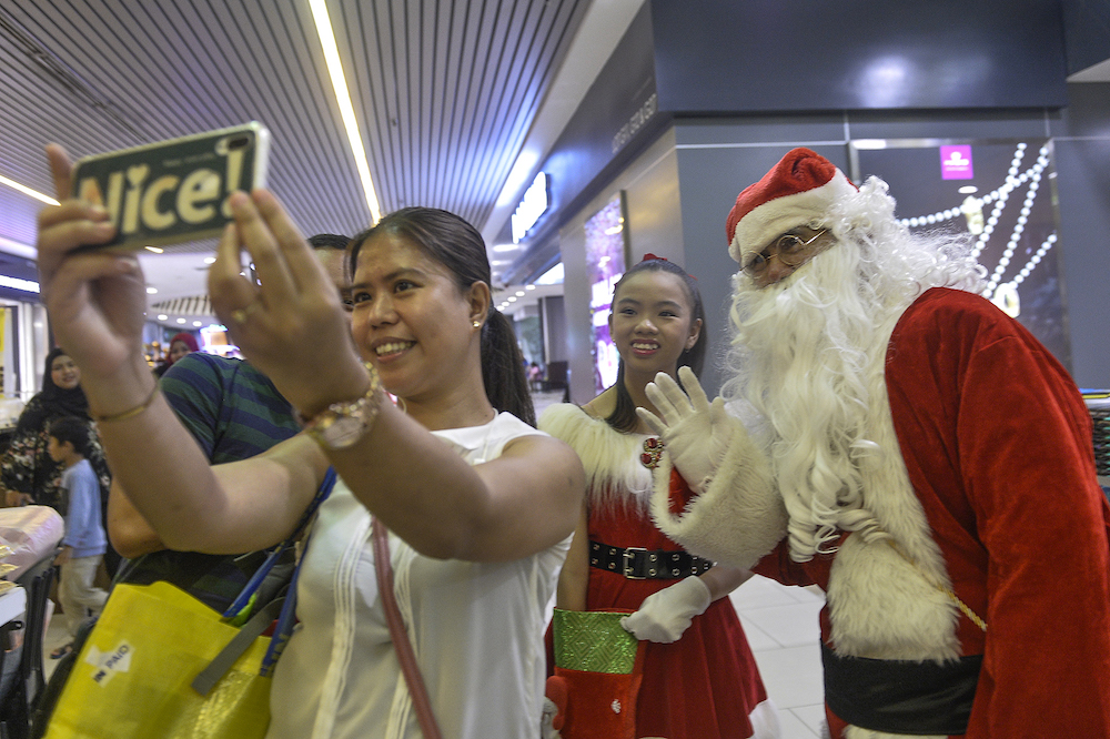 A man dressed as Santa Claus poses for a selfie with shoppers at Mydin USJ in Subang Jaya December 24, 2019. u00e2u20acu201d Picture by Miera Zuyana
